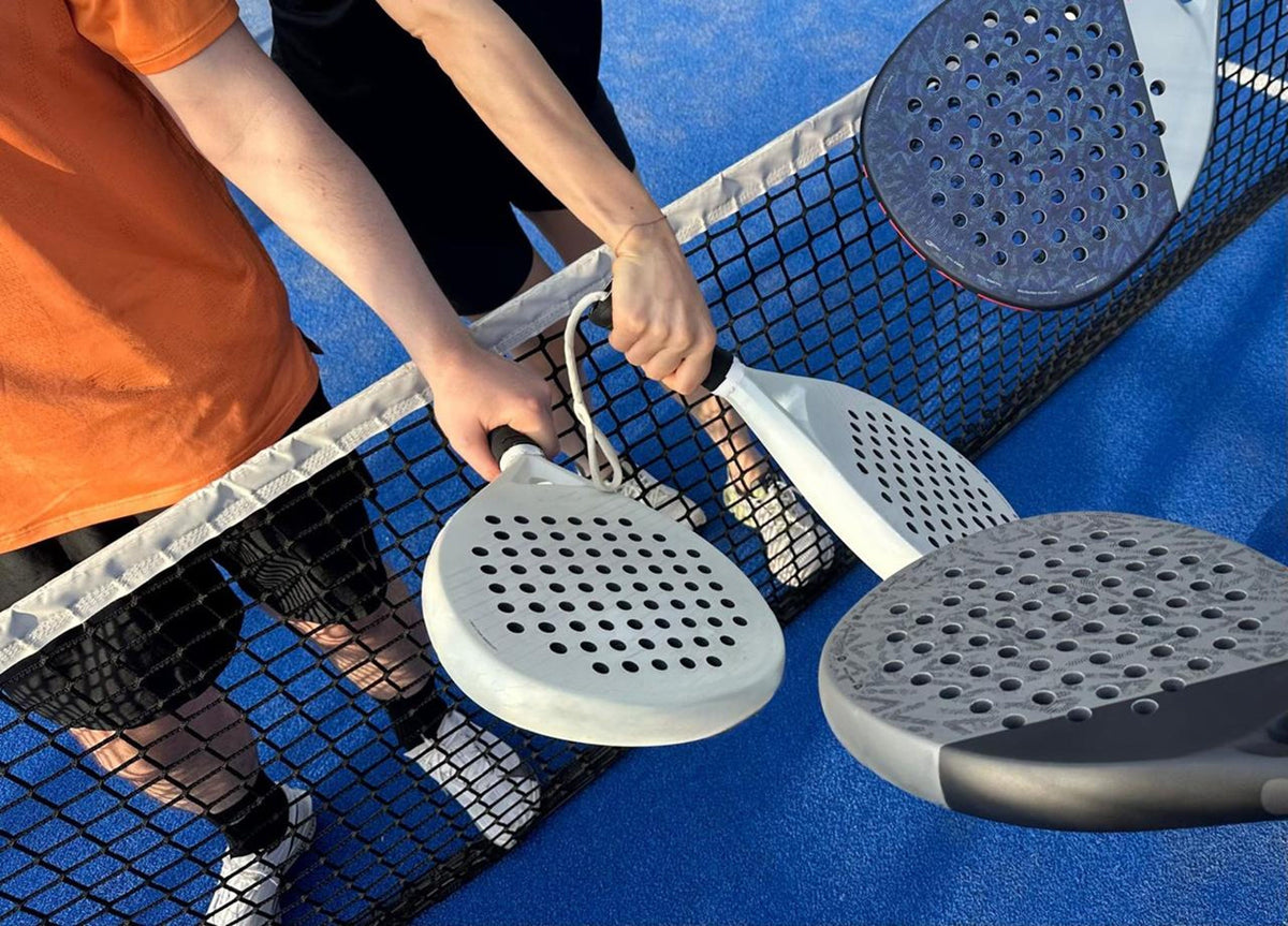 Zwei Padelspieler schlagen am Netz mit den Schlägern ab